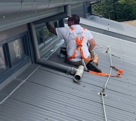 Painter on Colorbond roof painting a soffit with harness and lanyard