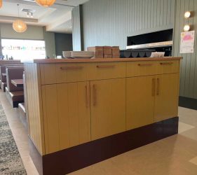 Close-up – Cupboard and counter with yellow paneling and a wall with green timber trim details.