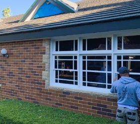 Painter applying white paint to the timber-framed windows of an outhouse at the Forestville