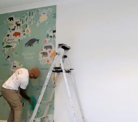 Installer applying world map mural wallpaper in Clovelly children’s room