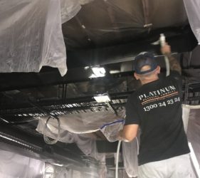 Platinum Painting crew member spraying new ceiling ductwork matte black while protecting heritage ceiling and timber beams in Surry Hills office
